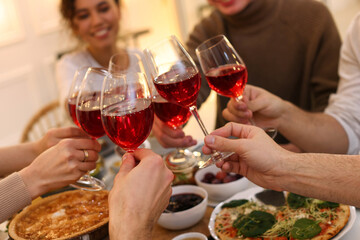 Group of people clinking glasses with red wine during brunch at table indoors, closeup