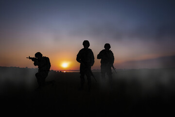 Fototapeta na wymiar Silhouettes of soldiers with machine guns on battlefield at sunset