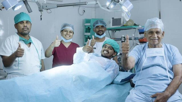 happy smiling Group of surgeons with patient showing thumbs up during surgery at operation theatre - concept approvel, healthcare and medical treatment