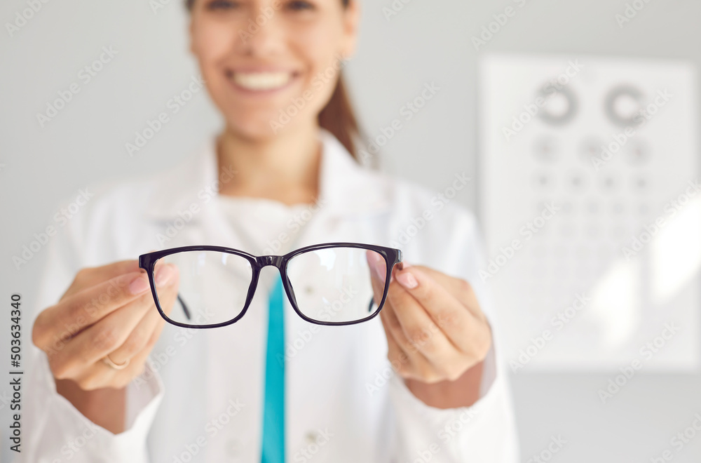 Wall mural close up of smiling woman optician offer glasses fir client or customer in optics salon. female doct