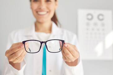 Close up of smiling woman optician offer glasses fir client or customer in optics salon. Female doctor recommend eyesight correction spectacles for good sight. Healthcare, medicine concept. - obrazy, fototapety, plakaty