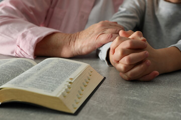 Boy and his godparent praying together at grey table, closeup