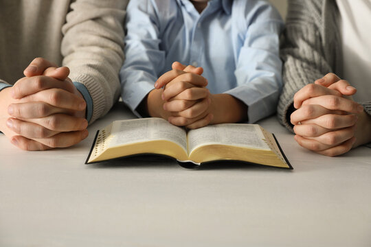 Boy and his godparents praying together at white wooden table, closeup