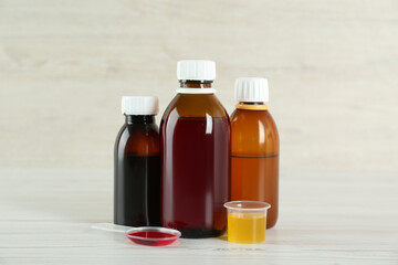 Bottles, spoon and measuring cup with cough syrup on white wooden table