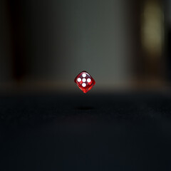 Closeup shot of a red dice showing the number five falling on the black table