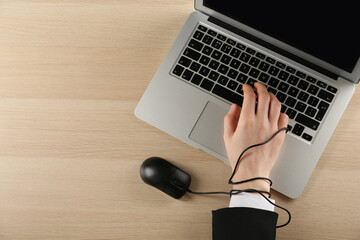 Internet addiction. Top view of man typing on laptop at wooden table, hand tied with computer mouse...