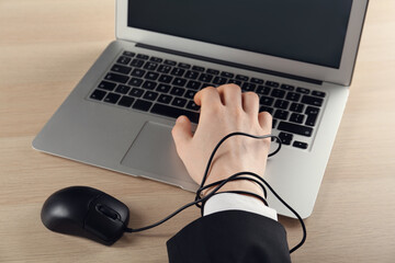 Internet addiction. Closeup view of man typing on laptop at wooden table, hand tied with computer...