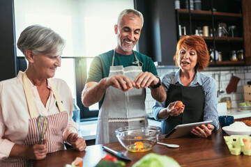 Group of senior friends at dinner party at home, cooking.