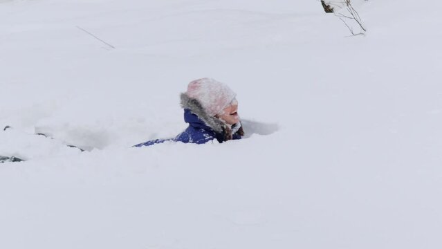 Happy young woman is having fun at winter day. She is diving into the snow in warm wear, 4k.