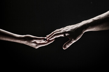 Obraz premium Two hands stretch each other, black background. Couple in love holding hads, close up. Helping hand, support, friendship.