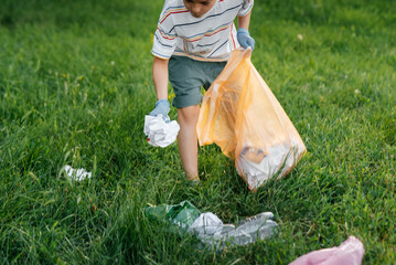A seven-year-old boy at sunset is engaged in garbage collection in the park. Environmental care,...
