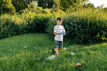 A seven-year-old boy at sunset is engaged in garbage collection in the park. Environmental care,...