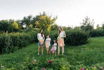 A group of adults and children together at sunset is engaged in garbage collection in the park....