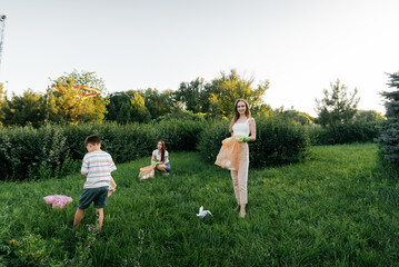 A group of adults and children together at sunset is engaged in garbage collection in the park. Environmental care, waste recycling. Sorting garbage.