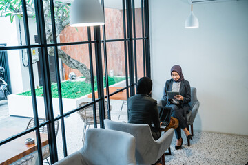 two muslim female worker sitting in sofa and using tablett pc
