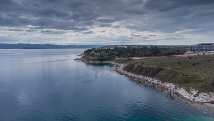 Fototapeta na wymiar Rocky beach around Savudrija or Alberi area viewed from above. Drone view of visible rocks leading into the blue sea on a cloudy day. Typical istrian rock formations and wild camping behind.
