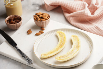 Two banana halves ready for peanut butter topping on white plate on marble board