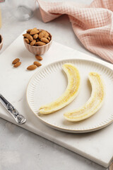 Two banana halves ready for peanut butter topping on white plate on marble board