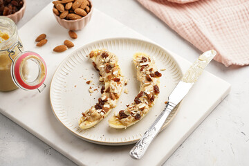 Two banana halves ready with peanut butter topping, raisins, almonds and chia seeds on white plate on marble board