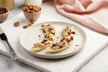 Two banana halves ready with peanut butter topping, raisins, almonds and chia seeds on white plate on marble board