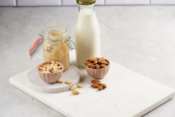 Peanuts, almonds in pink bowls, homemade peanut butter and almond milk on marble boards. Vegan food