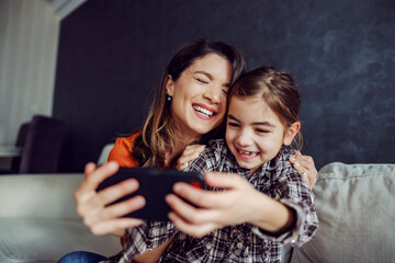 Smiling happy mother and daughter hugging and taking a selfie. 