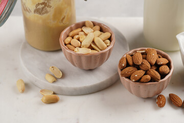 Peanuts, almonds in pink bowls, homemade peanut butter and almond milk on marble boards. Close-up on nuts