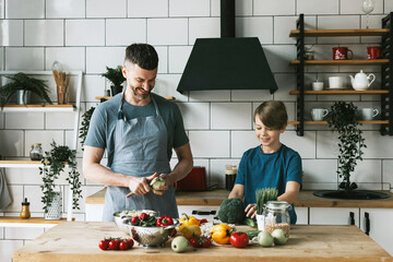 family dad young man and son teenage boy cook vegetable salad in kitchen and spend quality time...