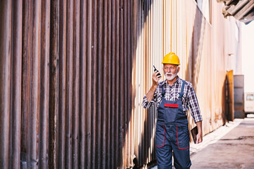 A senior supervisor walks around the factory yard and gives instructions to his workers on the walkie-talkie.