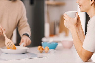 Close up of woman enjoying cup of coffee while a man preparing breakfast at home.
