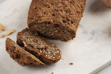 Homemade gluten-free and yeast-free buckwheat whole bread bread loaf with sunflower and pumkin seeds and nuts, cut in slices on white marble board