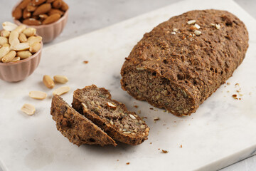 Homemade gluten-free and yeast-free buckwheat whole bread bread loaf with sunflower and pumkin seeds and nuts, cut in slices on white marble board