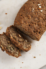 Homemade gluten-free and yeast-free buckwheat whole bread bread loaf with sunflower and pumkin seeds and nuts, cut in slices on white marble board