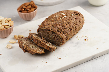 Homemade gluten-free and yeast-free buckwheat whole bread bread loaf with sunflower and pumkin seeds and nuts, cut in slices on white marble board