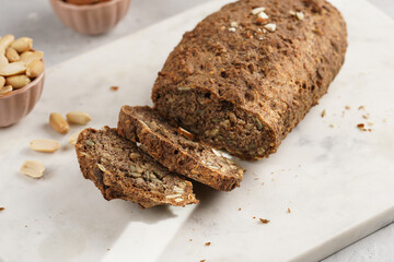 Homemade gluten-free and yeast-free buckwheat whole bread bread loaf with sunflower and pumkin seeds and nuts, cut in slices on white marble board, creative sun ray