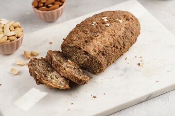 Homemade gluten-free and yeast-free buckwheat whole bread bread loaf with sunflower and pumkin seeds and nuts, cut in slices on white marble board, creative sun ray