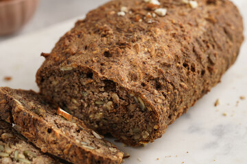 Homemade gluten-free and yeast-free buckwheat whole bread bread loaf with sunflower and pumkin seeds and nuts, cut in slices on white marble board, creative sun ray