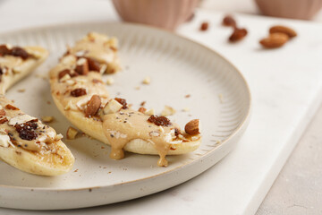 Two banana halves ready with peanut butter topping, raisins, almonds and chia seeds on white plate...