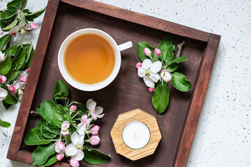 Cup of organic herbal tea on the wooden tray with napkin and blooming apple branches top view.
