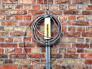 Aufgerolltes Stromkabel an einer senkrechten Kabelführung auf altem Mauerwerk aus rotbraunem Backstein eines Wohnhaus in Knokke-Heist an der Nordsee bei Brügge in Westflandern in Belgien