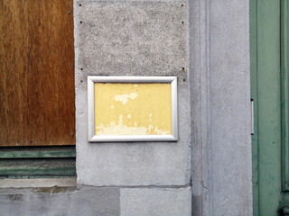 Obraz na płótnie Canvas Silberner Rahmen eines vergilbten gelben Schild auf grauem Stein eines Altbau in den Gassen der Altstadt von Brügge in Westflandern in Belgien