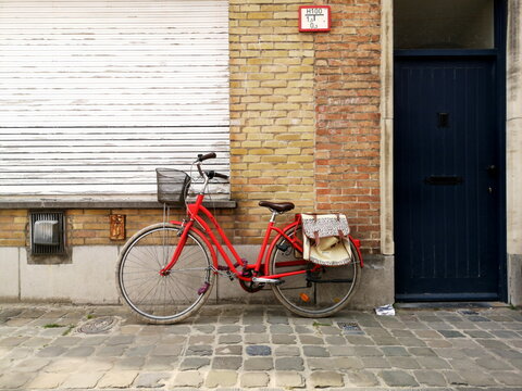Rotes BTWIN Damenrad oder Hollandrad mit Fahrradkorb und Satteltaschen vor Backsteinfassade auf Kopfsteinpflaster am 23.04.2022 in den Gassen der Altstadt von Br&uuml;gge in Westflandern in Belgien