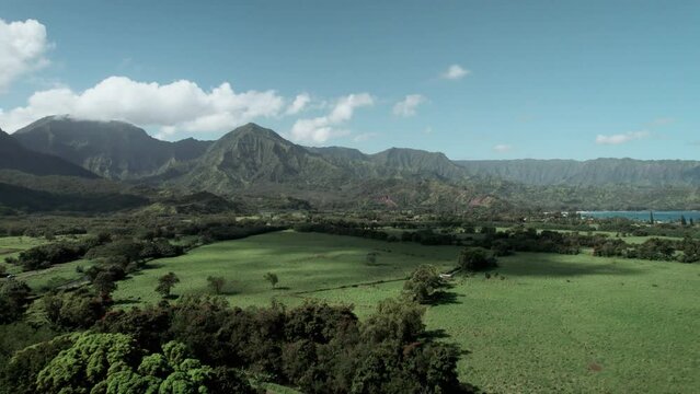 Fluffy clouds pass across tropical mountains above Hanalei Bay and Princeville, Kauai, aerial