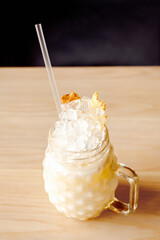 Cocktail pina colada with ice, cocktail tube and pineapple chips in glass with handle on wooden...