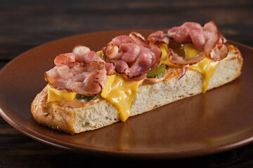 Crispy ciabatta bruschetta with bacon and melted cheese with sauce and pickles in a plate on a wooden table close-up. Horizontal orientation, no people. Focus on the foreground