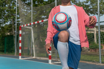 Image of a man tapping the ball with his knee. Close-up image of a young boy hitting the ball with his leg on a blue soccer field with the goal in the background.