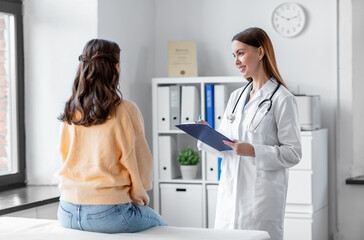 medicine, healthcare and people concept - smiling female doctor with clipboard talking to woman...