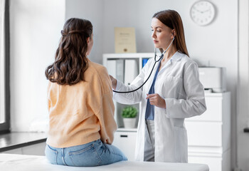 medicine, healthcare and people concept - female doctor with stethoscope listening to woman patient...
