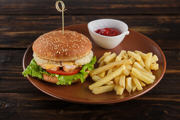 Homemade burger with juicy pineapple and chicken, tomatoes, cheese, sauce, lettuce leaves, French fries on a round plate against a dark wood background. Fast food. Horizontal orientation, copy space