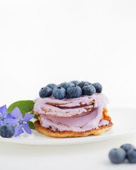 Pancakes with blueberries and yogurt on a white plate with violets flowers. White background with copy space 